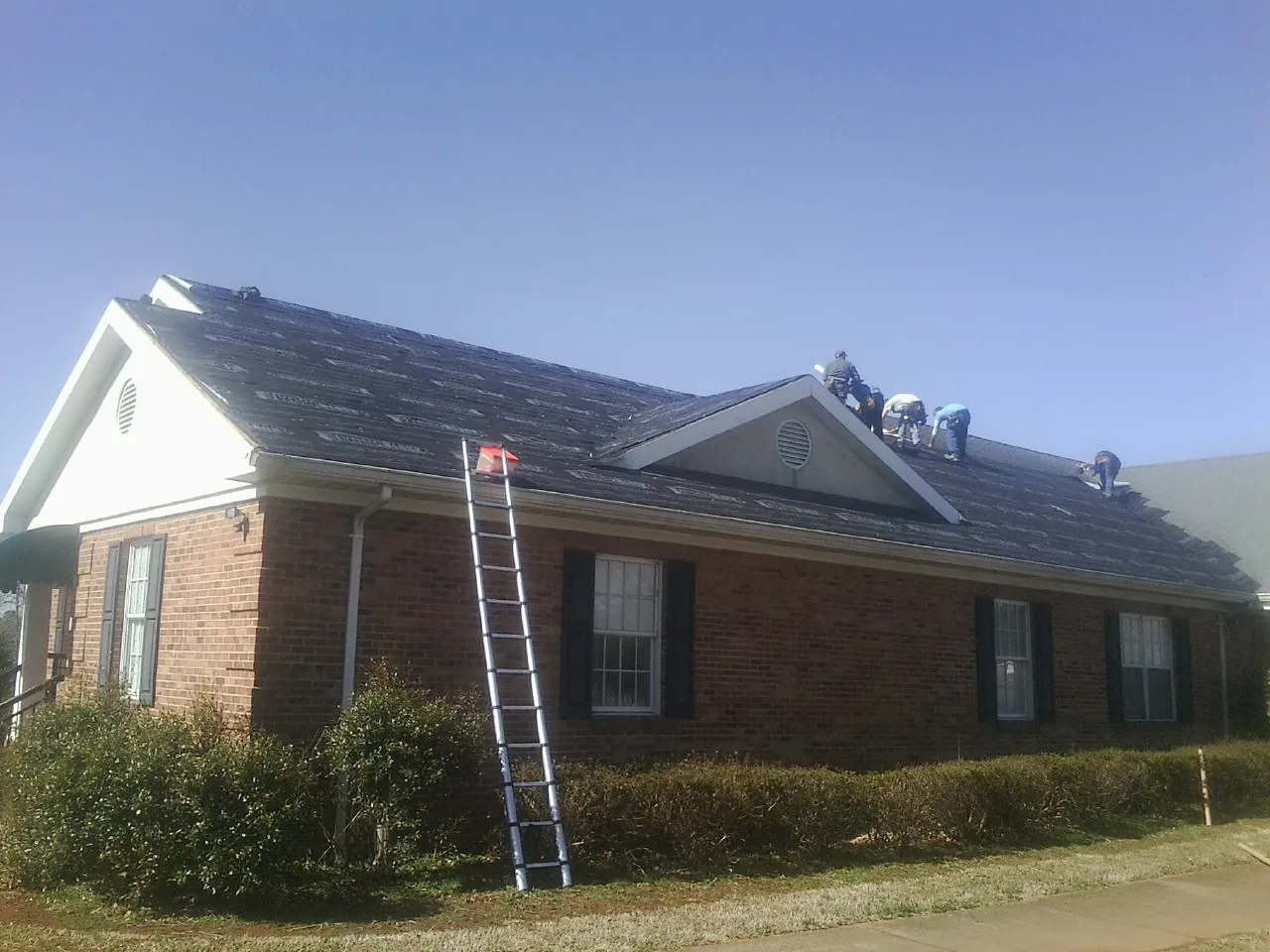 Crew tearing shingles off a brick ranch roof with a ladder set — Emergency Roof Repair work by our crew in Lebo