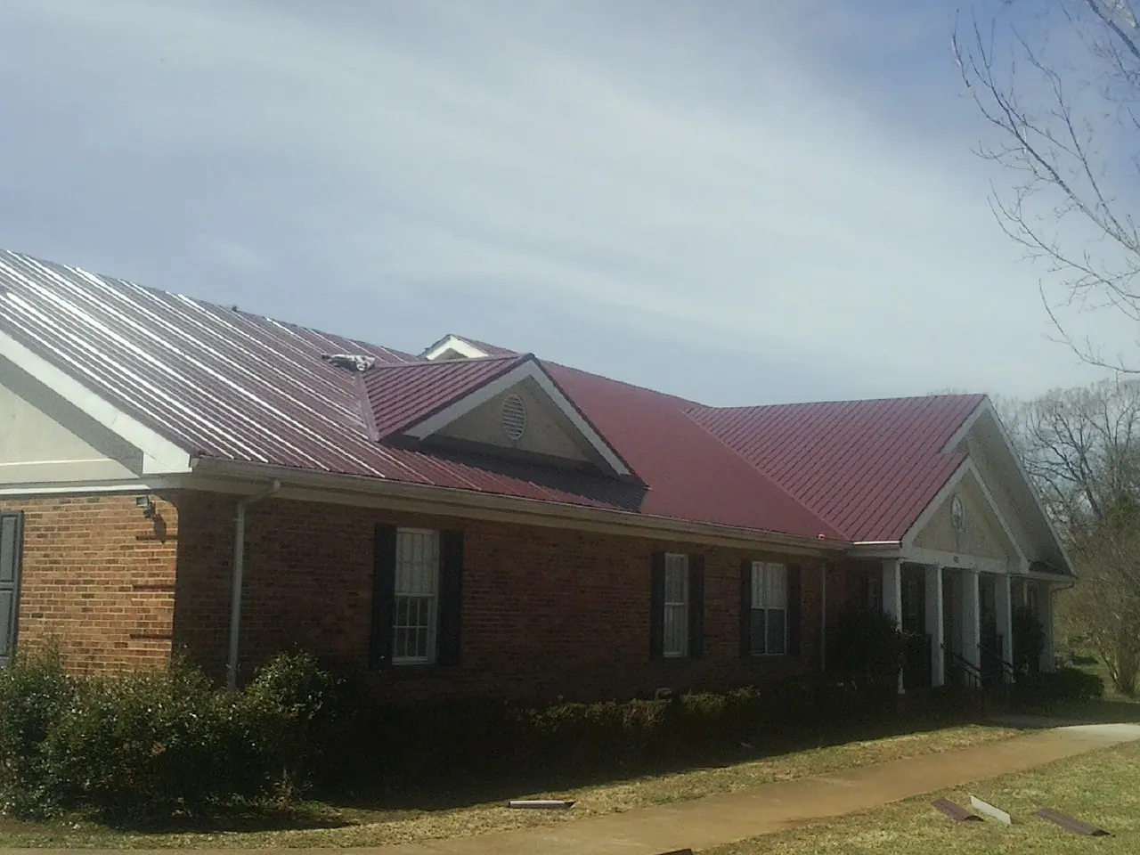 Red metal roof with gabled entries on a long brick building, from a Hail Damage Roof Repair job in Lebo