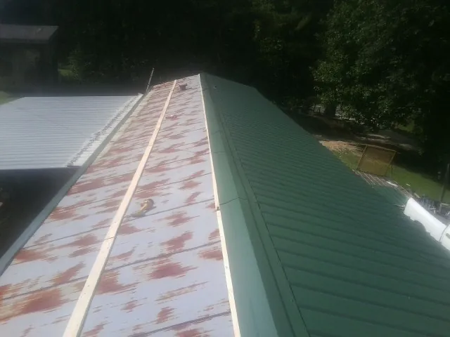 Old rusted panels beside newly installed green metal roofing — Wind Damage Roof Repair by Roofing Brothers in Lebo