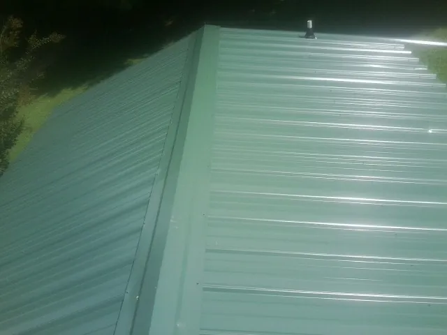 New green metal panels meeting at the ridge of a roof — Flat Roof Repair work by our crew in Lebo