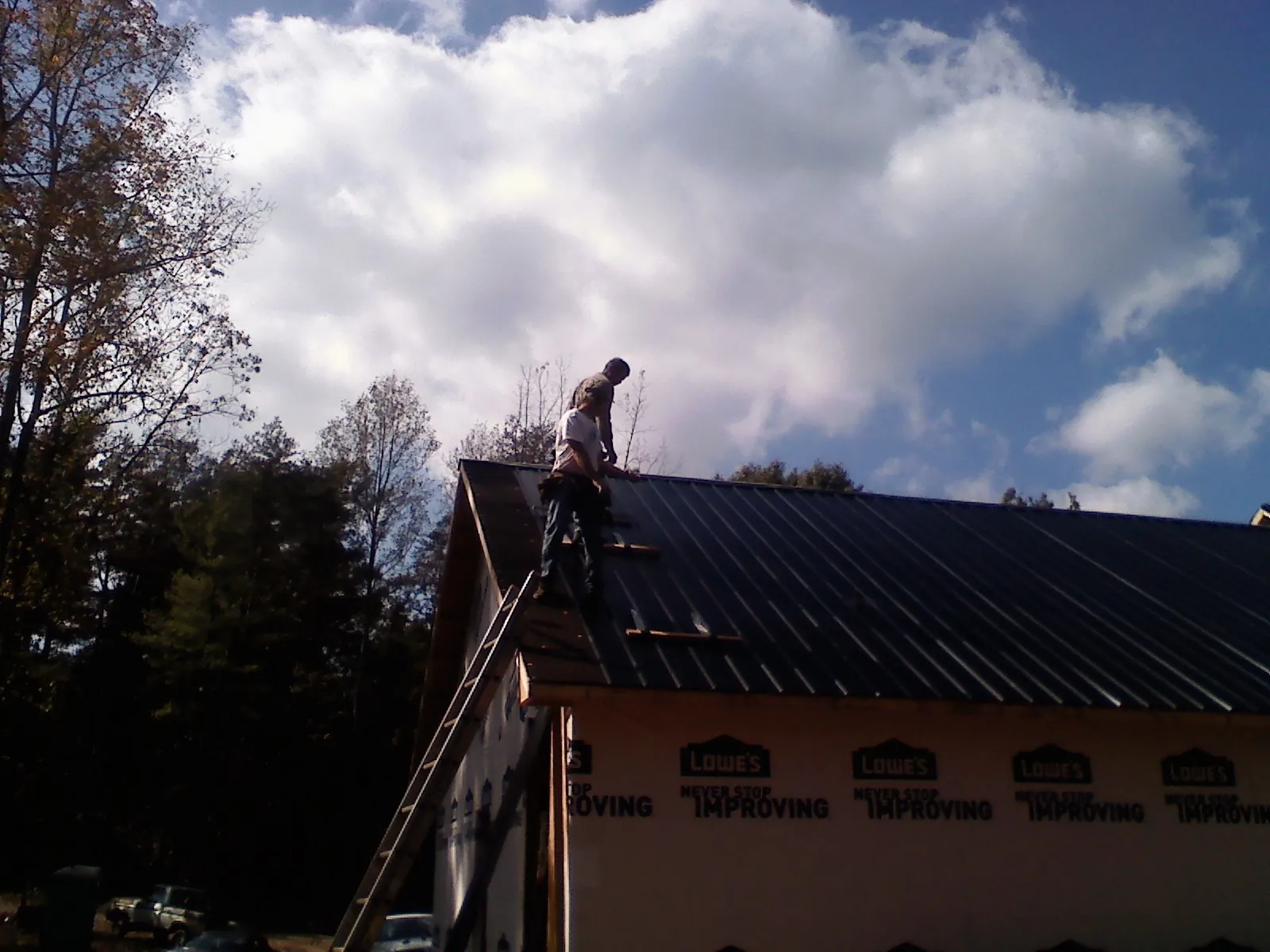 Roofer fastening dark metal panels high against a cloudy sky, from a Roof Inspection job in Lebo