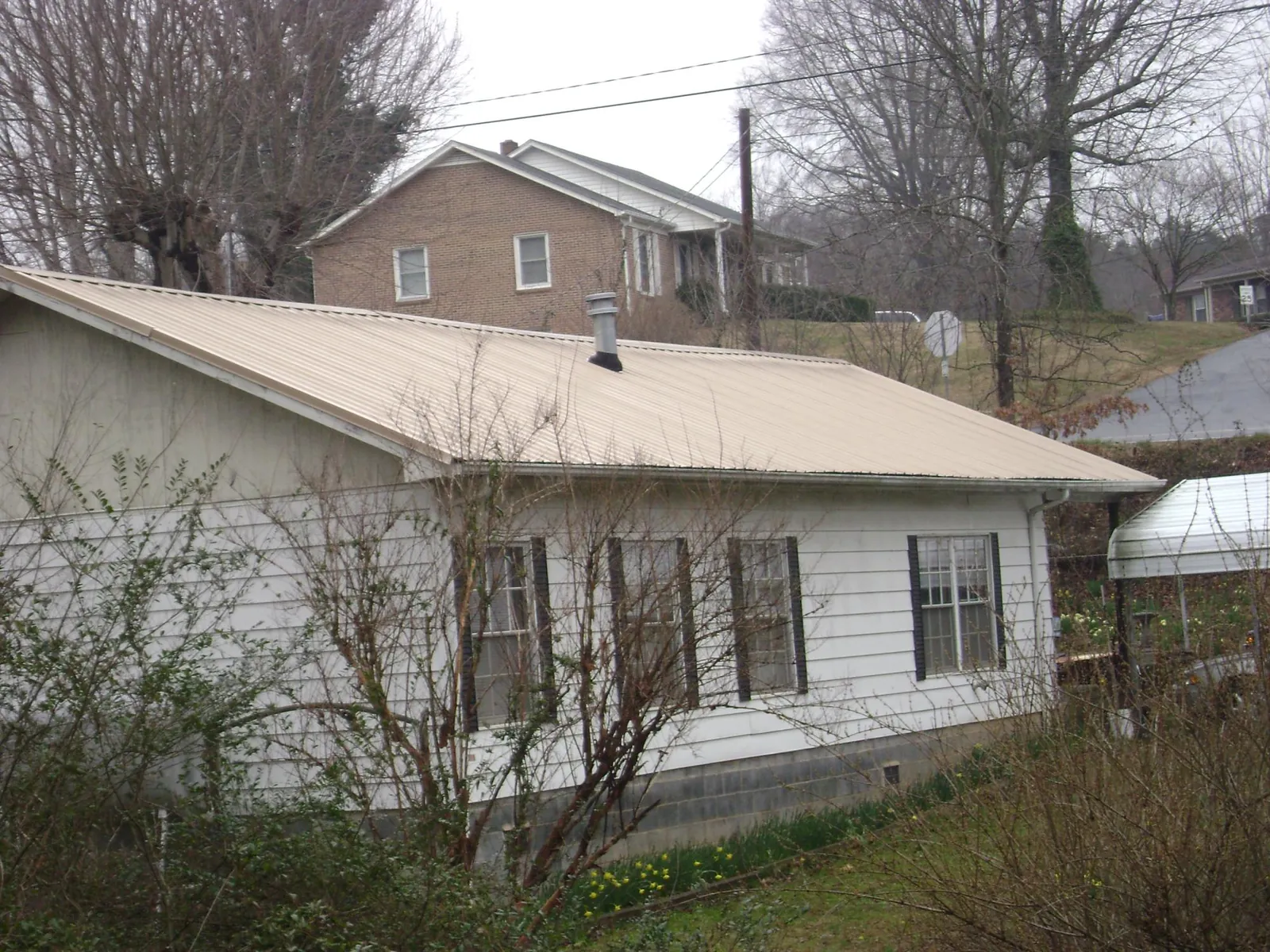 Tan metal roof on a white sided house set into a hillside — Commercial Roofing by Roofing Brothers in Lebo