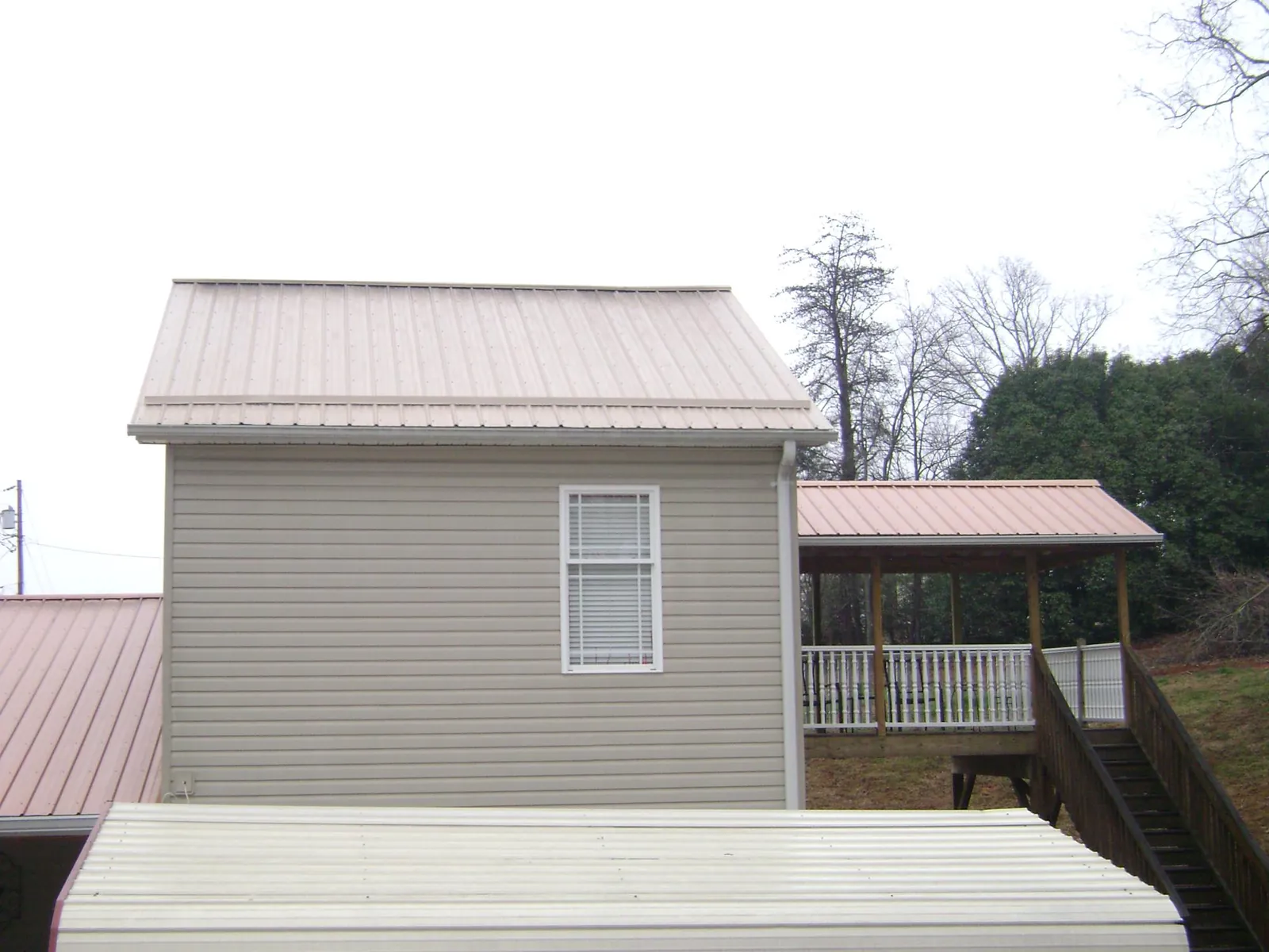 Tan metal roofs on a two story addition and attached porch, from a Roof Replacement job in Lebo